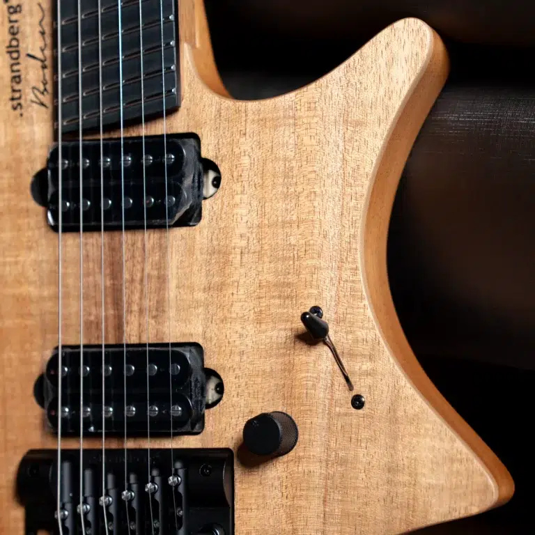 Close-up of a natural wood electric guitar body with two black humbucker pickups, a volume knob, and a toggle switch. ขายราคาพิเศษ