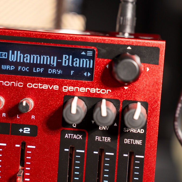 Close-up of a red octave generator guitar effects pedal with a small digital display and knobs labeled Q, ENV, ATTACK, FILTER, SPREAD, and DETUNE. ขายราคาพิเศษ