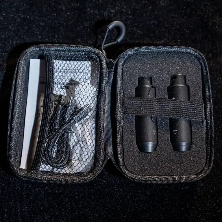 Two small black binoculars secured in foam padding inside a zipped travel case, with cables and accessories in the left pocket. ขายราคาพิเศษ