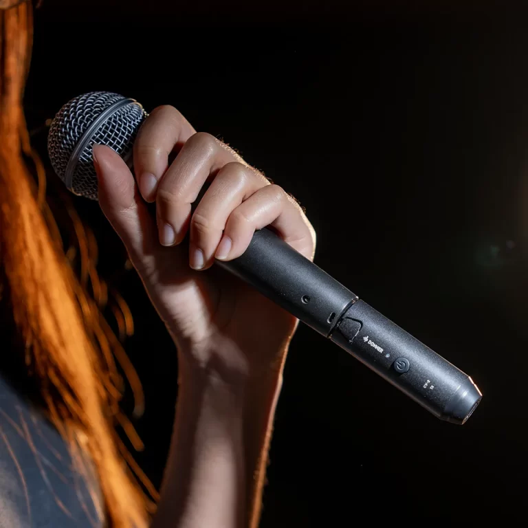 Close-up of a hand gripping a wireless microphone on a dark stage background. ขายราคาพิเศษ