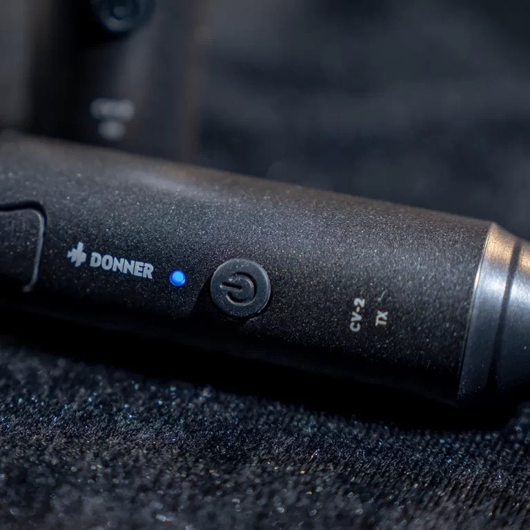 Close-up of a Donner microphone body with a blue power indicator light on a dark surface. ขายราคาพิเศษ
