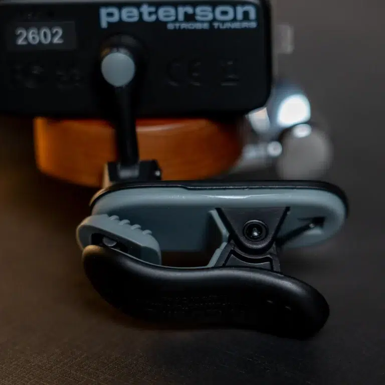 Close-up of a clamp and swivel mount attached to a black device labeled Peterson Strobe Tuners, showing a gear-like hinge in the foreground. ขายราคาพิเศษ