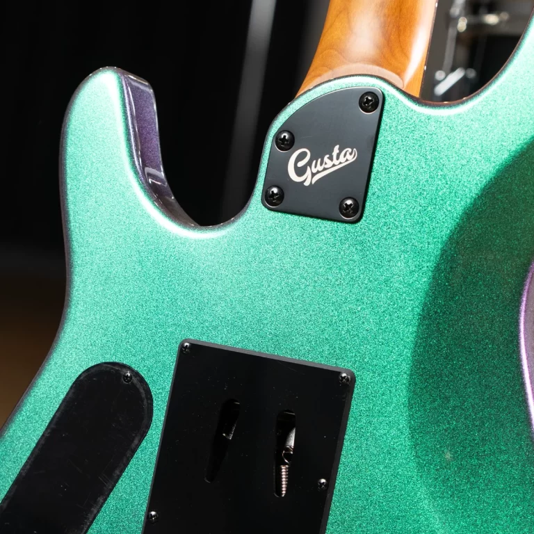Close-up of a sparkly green electric guitar body with a black backplate reading 'Gusta' near the neck heel and a black pickguard below. ขายราคาพิเศษ