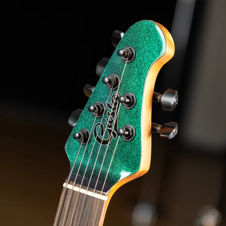 Close-up of a glittery green guitar headstock with six tuning pegs and strings intact on a wooden neck field. ขายราคาพิเศษ