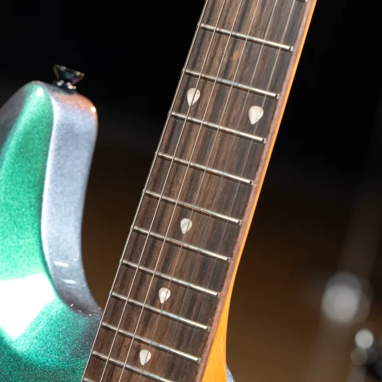 Close-up of a green guitar body and wooden fretboard with metal frets and white dot inlays. ขายราคาพิเศษ