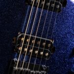 Close-up of gold guitar strings over black humbucker pickups on a blue glittery electric guitar body with a metal bridge. ขายราคาพิเศษ