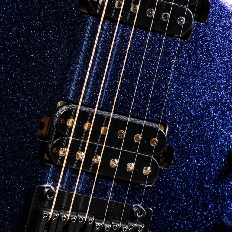 Close-up of gold guitar strings over black humbucker pickups on a blue glittery electric guitar body with a metal bridge. ขายราคาพิเศษ