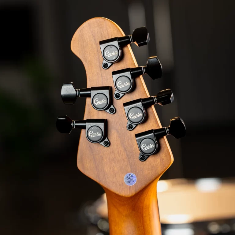 Close-up of a guitar headstock with six black tuning pegs, wood grain neck visible and 'Gusta' logos on the pegs ขายราคาพิเศษ