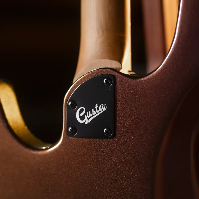 Close-up of a brown electric guitar body showing the black neck plate with the word 'Gusta' and four screws. ขายราคาพิเศษ