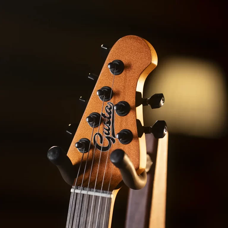 Close-up of an orange guitar headstock with tuning pegs and strings, set against a dark blurred background. ขายราคาพิเศษ
