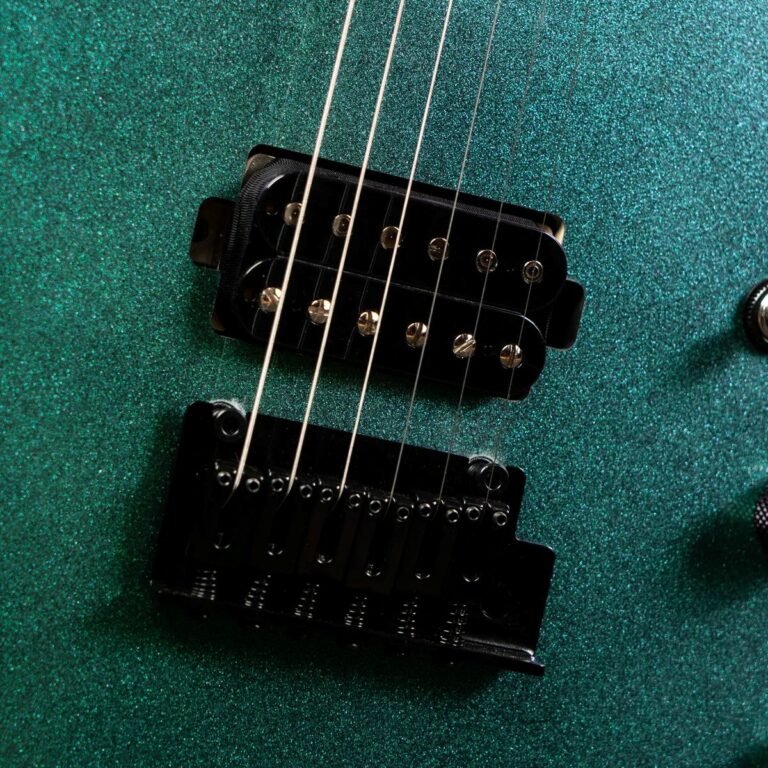 Close-up of an electric guitar's two black pickups and six strings on a teal glittery body. ขายราคาพิเศษ