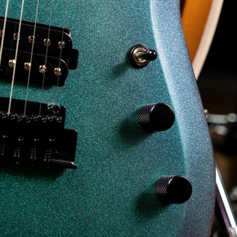 Close-up of a glittery teal-green electric guitar body with a pickup, toggle switch, and three black knobs. ขายราคาพิเศษ