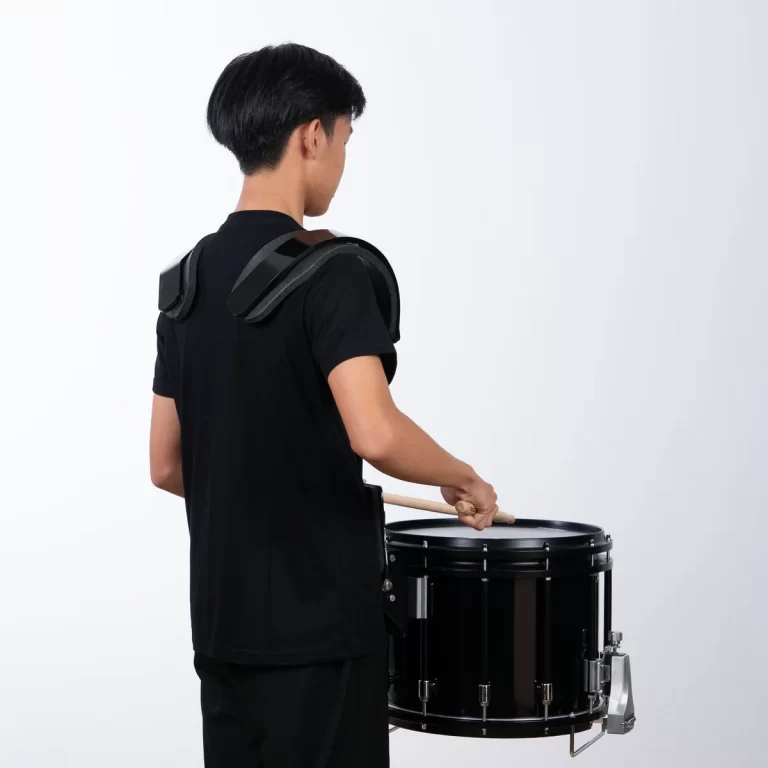 Back view of a person wearing a black drum shoulder harness, striking a black snare drum with drumsticks ขายราคาพิเศษ