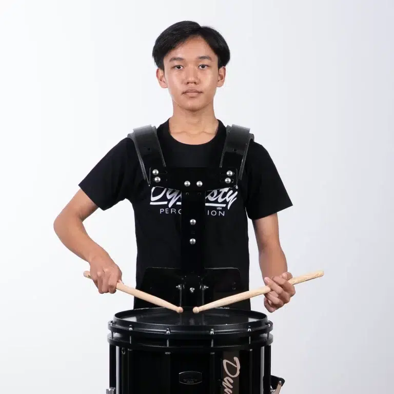 Young person wearing a black drum harness and playing a bass drum with drumsticks ขายราคาพิเศษ