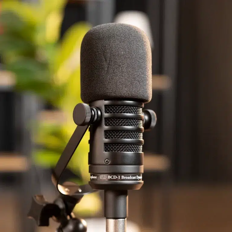 Close-up of a studio microphone with a foam windscreen mounted on a stand in a recording setup. ขายราคาพิเศษ
