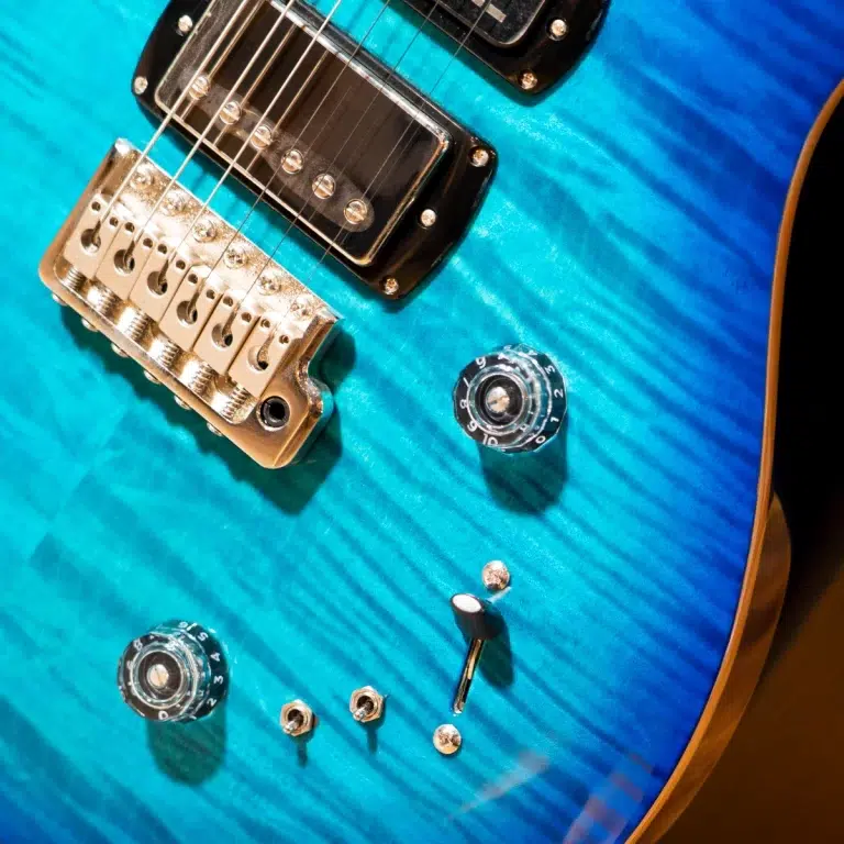 Close-up of a blue electric guitar showing the chrome bridge, pickup, and control knobs.