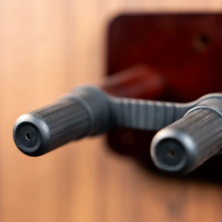 Close-up of two gray textured gym handles extending toward the viewer, connected by a curved bar, with a blurred wooden background behind. ขายราคาพิเศษ