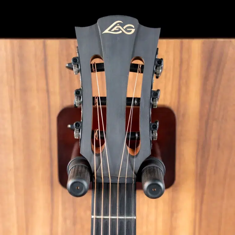 Close-up of a guitar headstock viewed from above, showing tuning pegs, strings, and a logo on a dark headstock against a wooden background ขายราคาพิเศษ