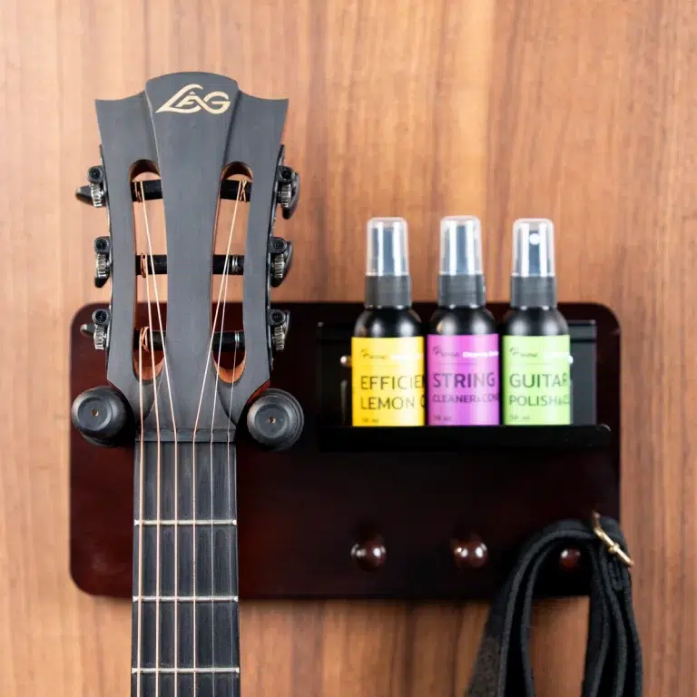 Headstock of a guitar mounted on a wall with a small shelf holding three spray bottles labeled Lemon Cleaner, String Cleaner, and Guitar Polish (guitar care set). ขายราคาพิเศษ