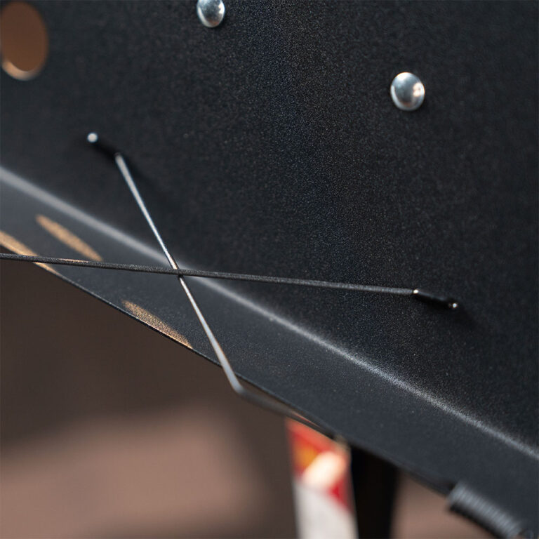 Close-up of a dark metallic panel with two thin wires crossing diagonally and small rivets visible on the surface. ขายราคาพิเศษ