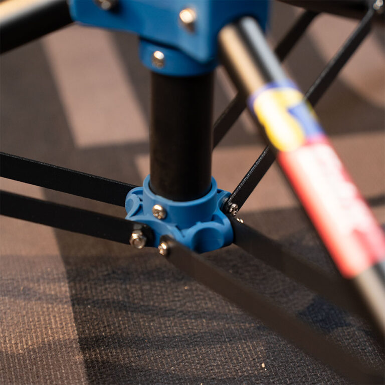 Close-up of a blue plastic joint with black rods forming a small quad-rotor frame on a dark surface ขายราคาพิเศษ