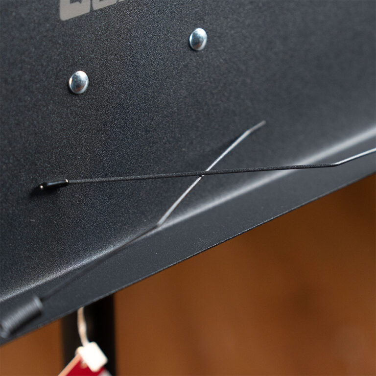 Close-up of a black textured metal panel with two screws and a thin diagonal wire stretched across it. ขายราคาพิเศษ