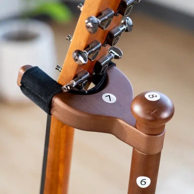 Close-up of a classical guitar headstock with tuning pegs resting on a wooden surface, a chair-like support with a white '1' sticker visible. Numerical '6' sticker on the chair leg also visible in the foreground. ขายราคาพิเศษ