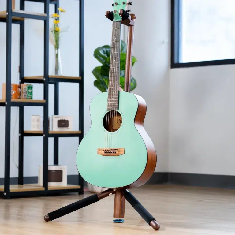 Mint green acoustic guitar on a wooden stand in a bright room with shelves and plants nearby. ขายราคาพิเศษ