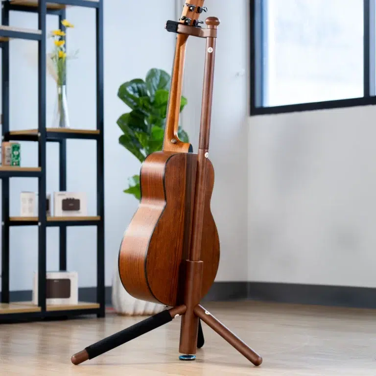 Wooden acoustic guitar resting on a tripod stand in a bright room with shelves and a plant nearby. ขายราคาพิเศษ
