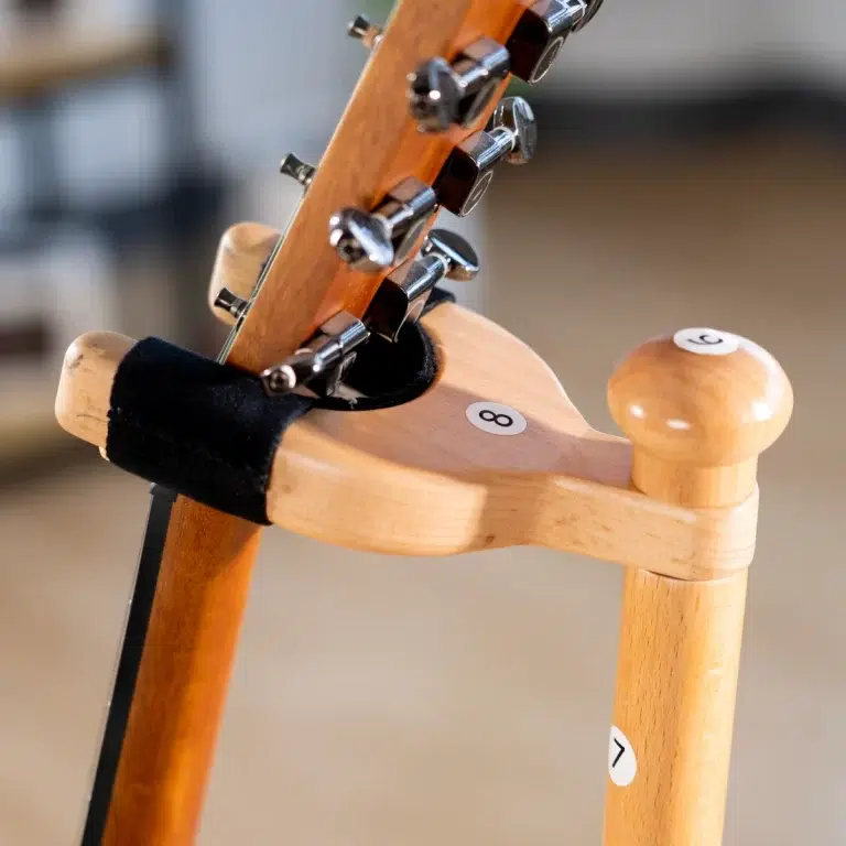 Close-up of a guitar neck and tuning pegs resting on a light wooden stand with numbered stickers (8 and 7). ขายราคาพิเศษ