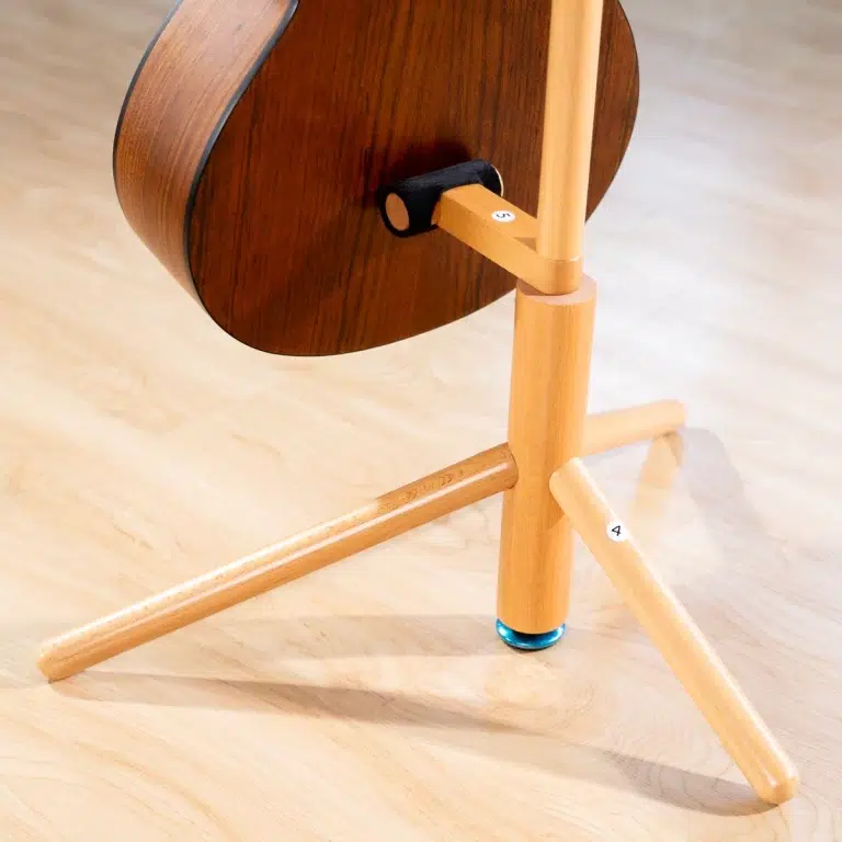 Side view of a small acoustic guitar on a light wood tripod stand with numbered joints visible (4 and 5). ขายราคาพิเศษ