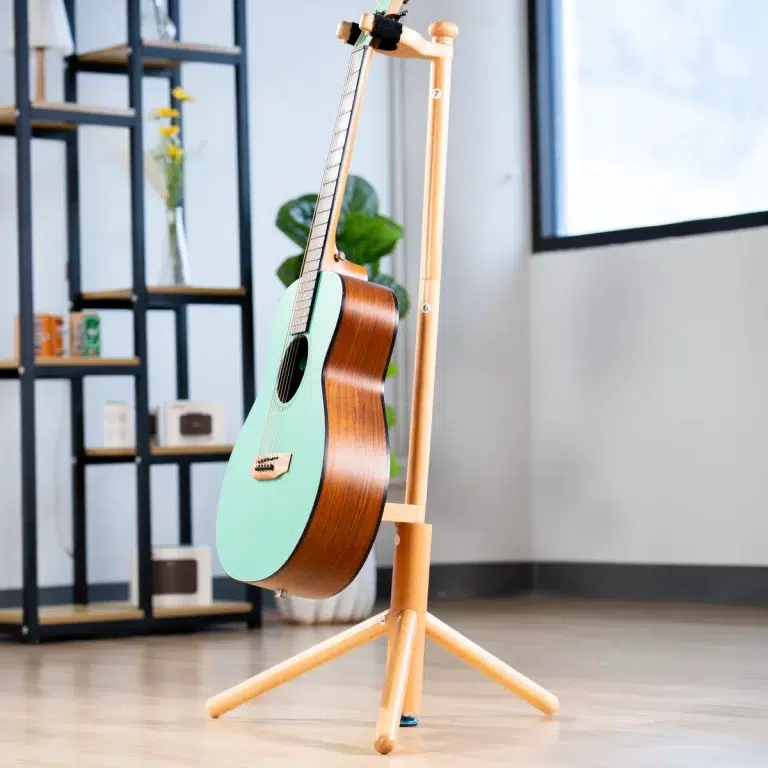 Mint green acoustic guitar on a wooden stand in a sunlit, modern room with shelves in the background. ขายราคาพิเศษ
