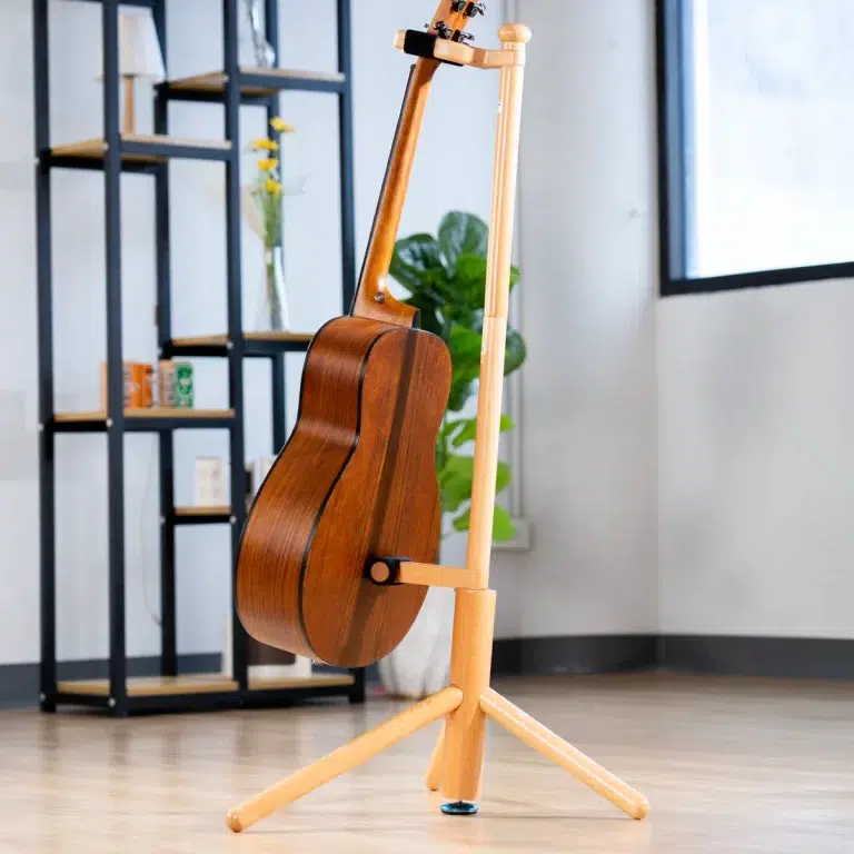 Acoustic guitar resting on a light wood stand in a bright living room with shelves and a plant in the background. ขายราคาพิเศษ