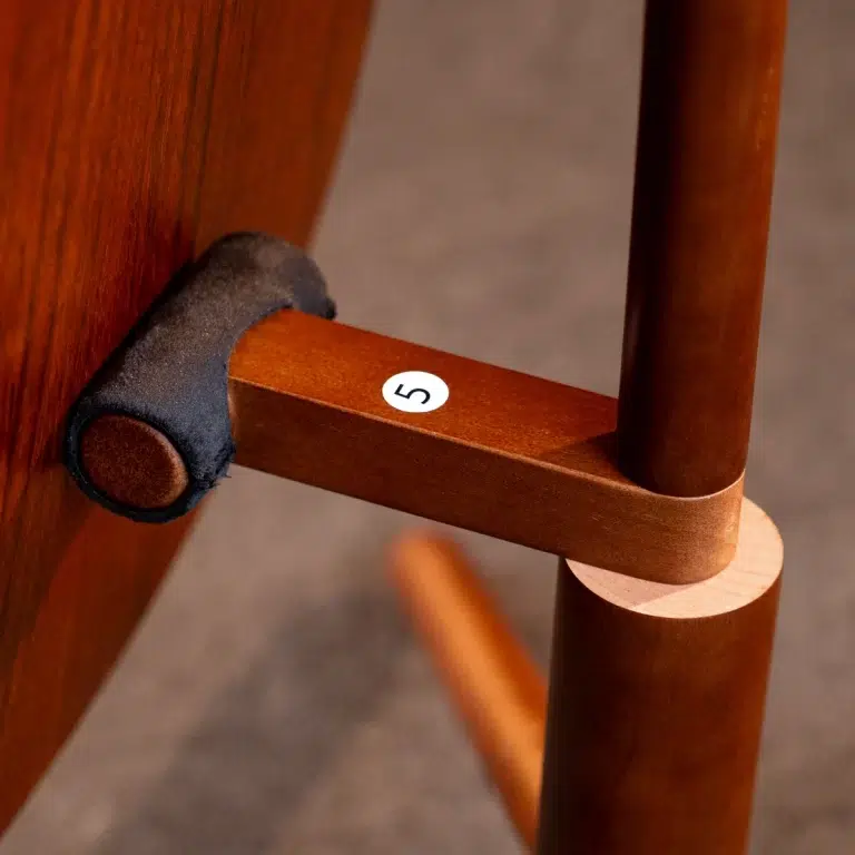 Close-up of a wooden chair joint with a small white circular sticker showing the number 5 on the connecting bar. ขายราคาพิเศษ