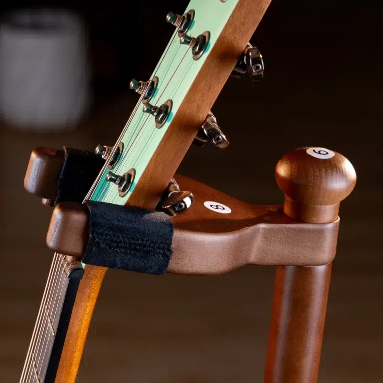 Close-up of a guitar headstock with six tuning pegs, mint green fretboard, resting on a wooden stand. ขายราคาพิเศษ