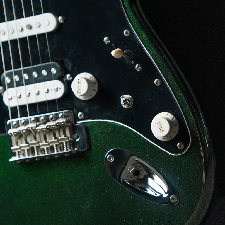 Close-up of a green electric guitar showing pickups, knobs labeled Tone and Volume, bridge, and input jack on a black pickguard. ขายราคาพิเศษ