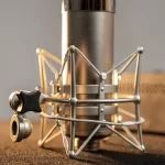 Close-up of a metal studio microphone mounted in a spider-style shock mount on a recording desk. ขายราคาพิเศษ