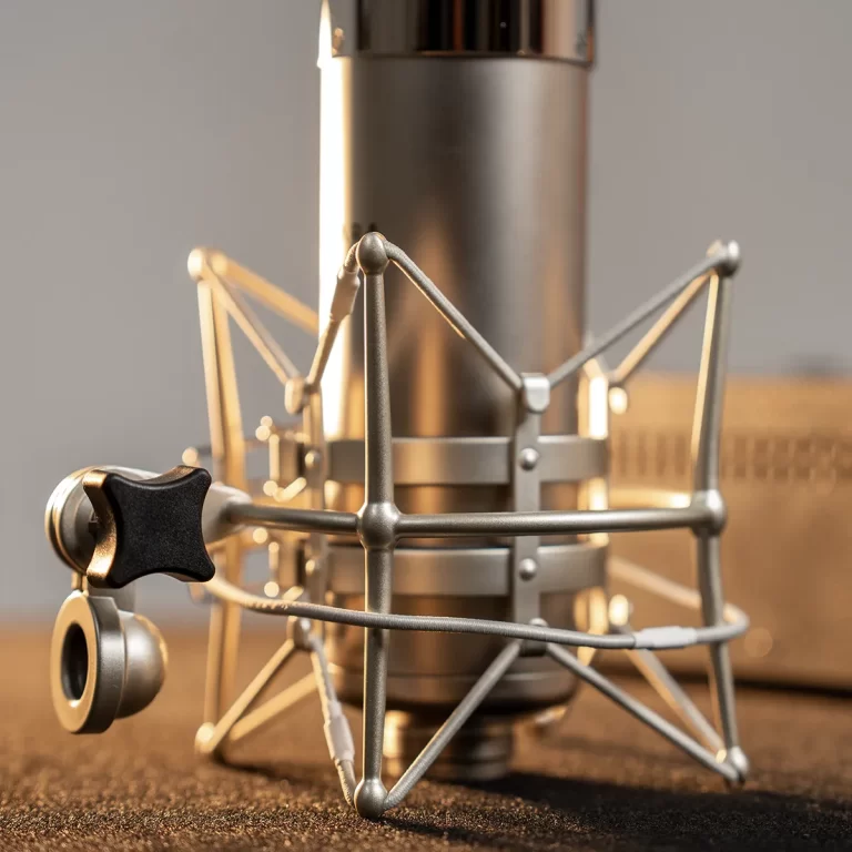 Close-up of a metal studio microphone mounted in a spider-style shock mount on a recording desk. ขายราคาพิเศษ