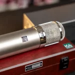 Close-up of a silver studio microphone with a woven mesh grille resting on a red wooden case labeled KA-47. ขายราคาพิเศษ