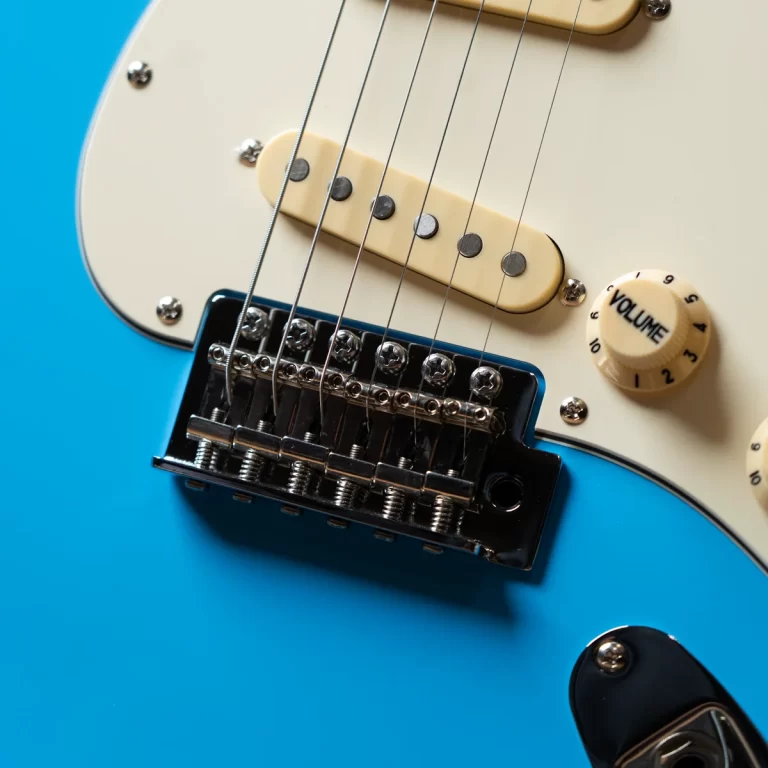 Close-up of a blue electric guitar showing cream pickguard, strings, pickups, and a volume knob. ขายราคาพิเศษ