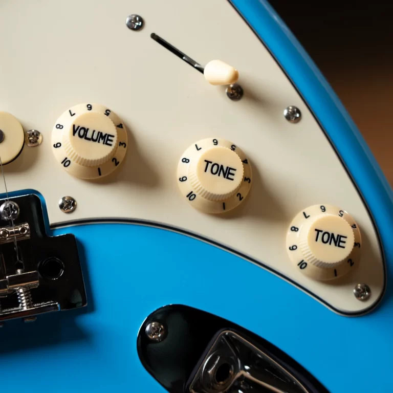 Close-up of a blue electric guitar showing volume and tone knobs on a white pickguard. ขายราคาพิเศษ