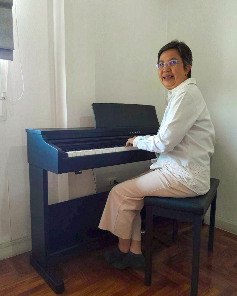 Person sitting at a dark blue upright piano, hands on the keys, in a bright room.