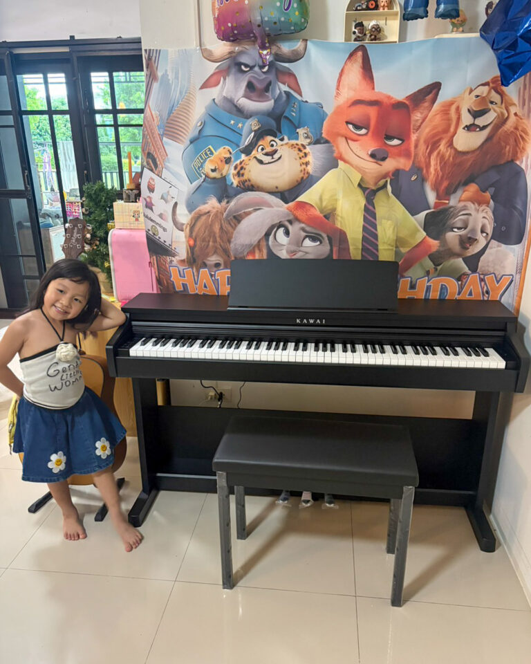 Young girl posing beside a black Kawai upright piano in a room with a colorful animal-themed backdrop.
