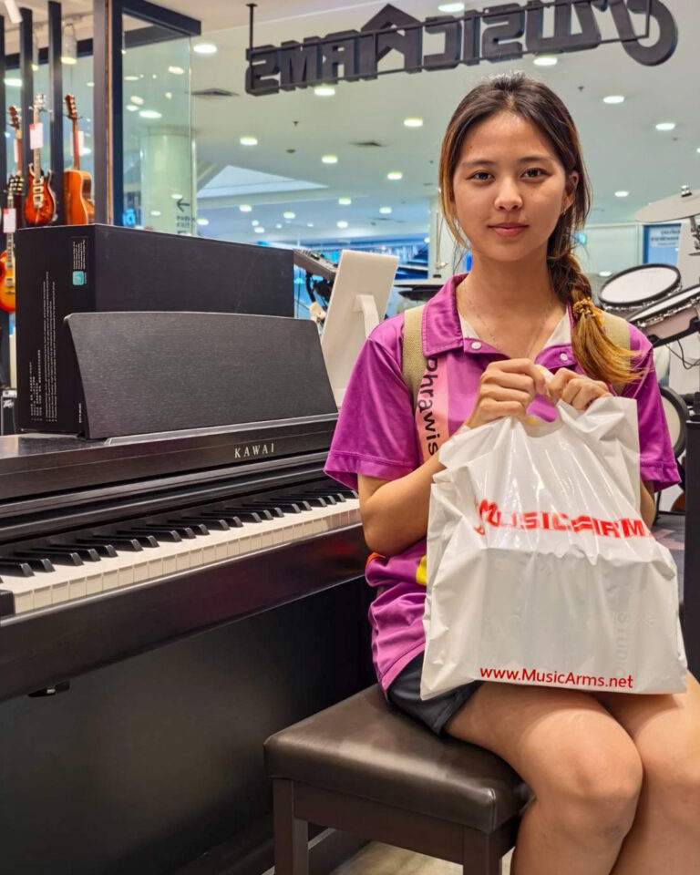 Young woman sits on a piano bench in a music store, holding a white MusicArms bag in front of a Kawai piano.