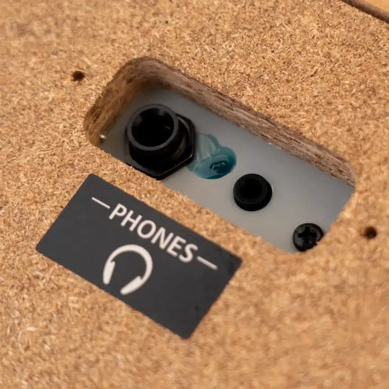 Close-up of a wall panel recessed in corkboard showing a phone jack and two other ports, next to a black sign reading 'PHONES' with a headset icon. ขายราคาพิเศษ