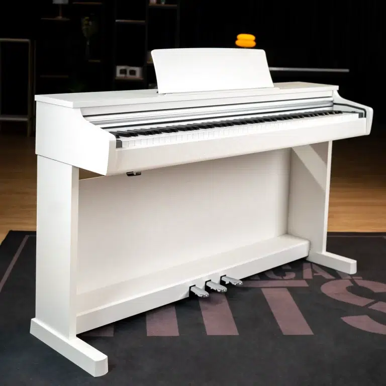 White upright piano in a showroom, viewed from the side with pedals visible and a sheet music stand on top of the keyboard. ขายราคาพิเศษ
