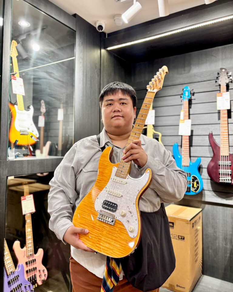 Person in a guitar shop holding an orange sunburst electric guitar with a white pickguard.
