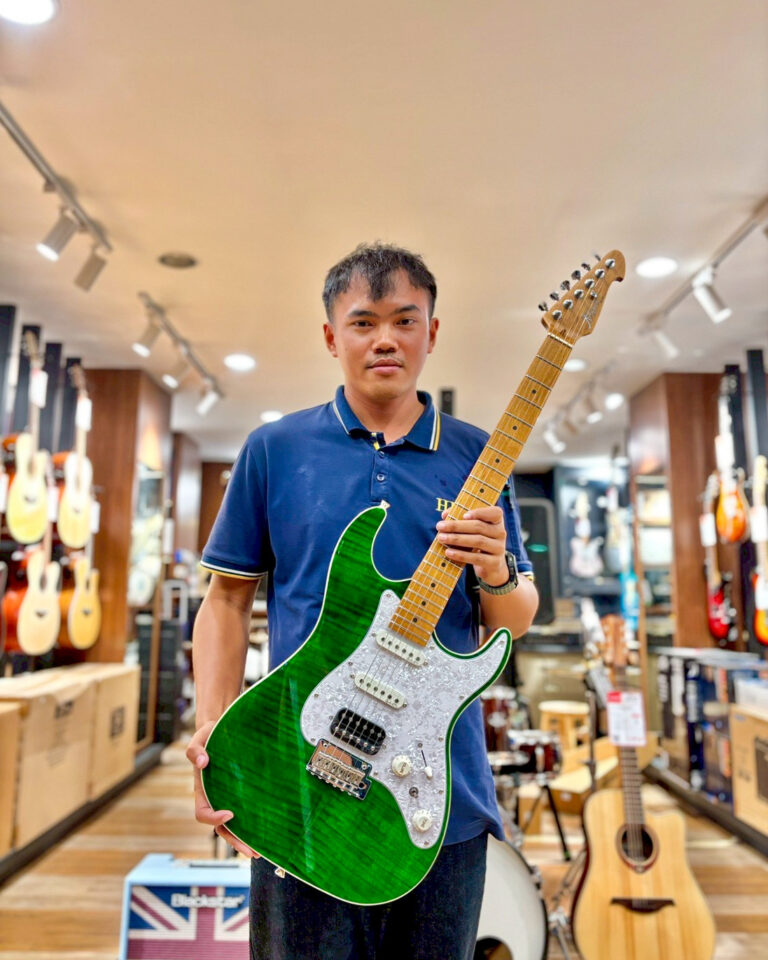 Young man in a guitar shop holding a bright green electric guitar with a white pearloid pickguard.