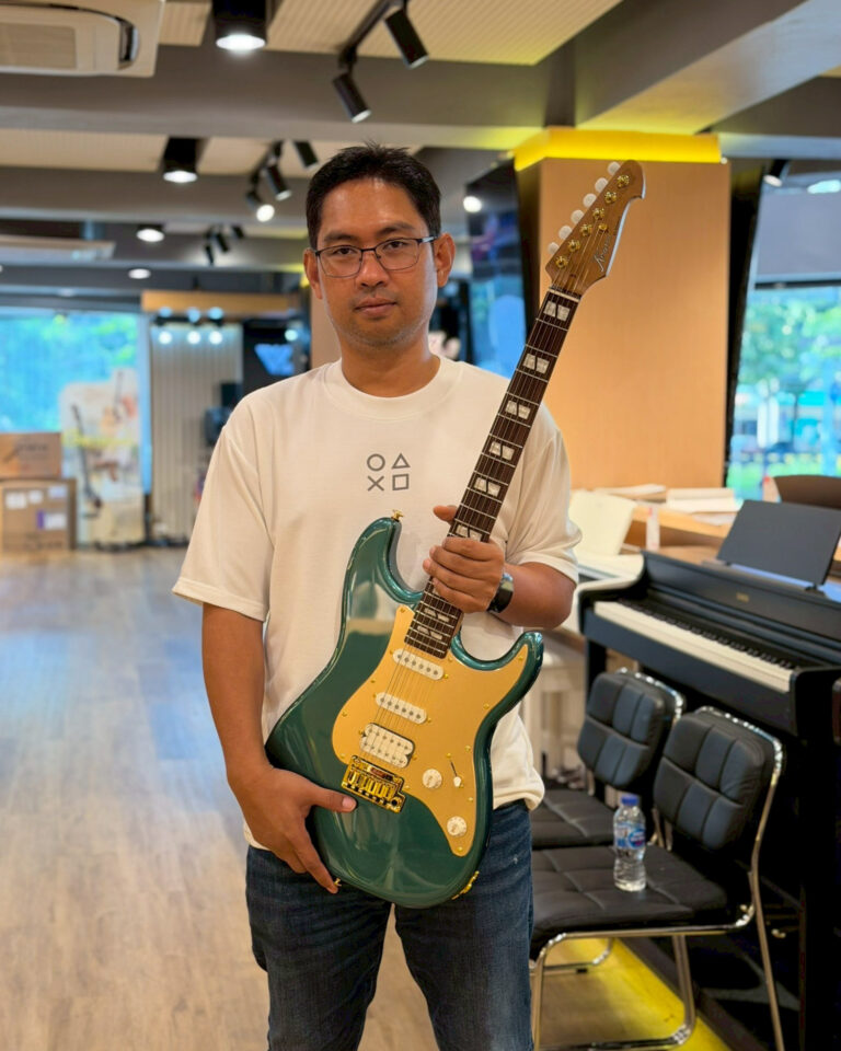 Man in a white T-shirt holding a green electric guitar inside a music store