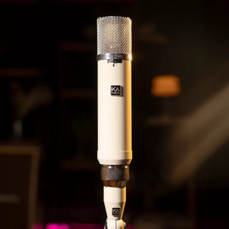 Close-up of a white studio microphone with a metallic grille, standing upright in a dim recording studio. ขายราคาพิเศษ